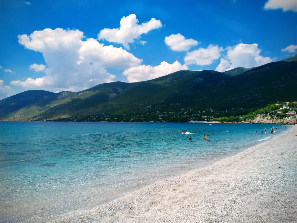 Swimmers in the calm, clear water of a pebble beach near Porto Germeno, with mountains behind