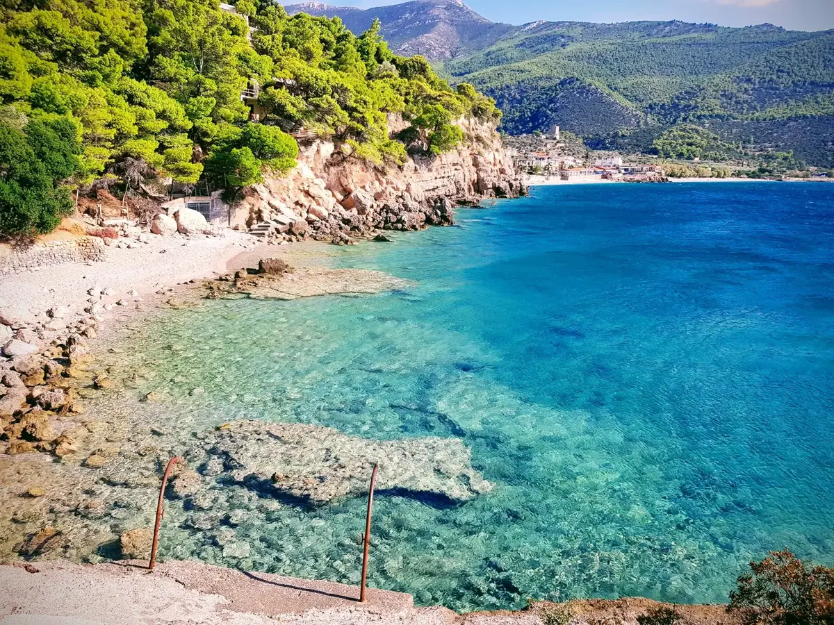Secluded pine-fringed cove with turquoise water and a rocky entry point near Porto Germeno