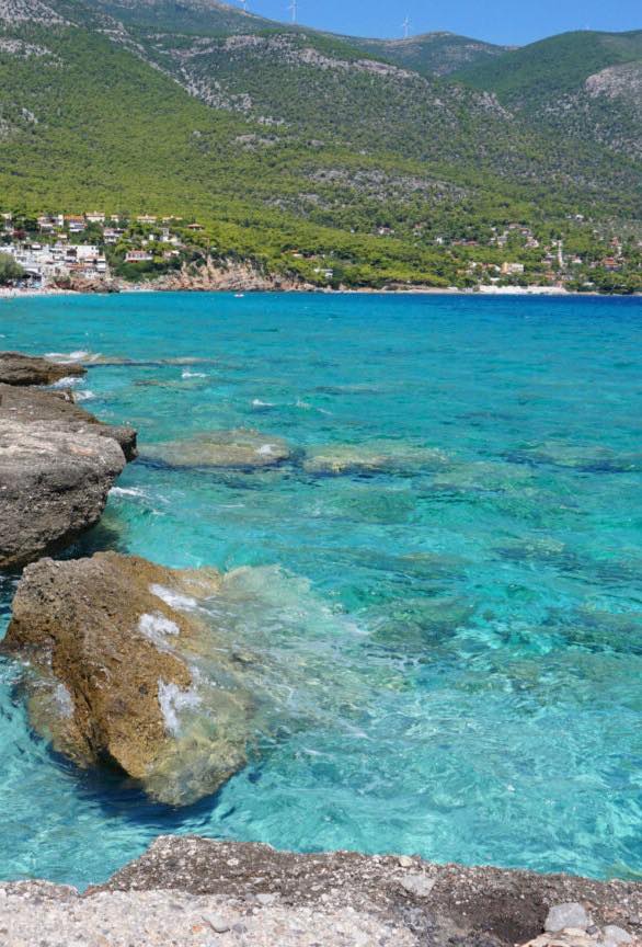Καθαρά γαλαζοπράσινα νερά σε βραχώδη ακτή κοντά στο Πόρτο Γερμενό, με το χωριό στο βάθος