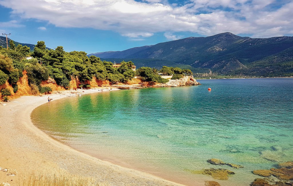Secluded turquoise cove near Porto Germeno with pine trees and red cliffs